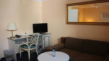Ein Hotelzimmer mit Schreibtisch, Stuhl, Fernseher, Sofa und einem runden Tisch mit einer Flasche.