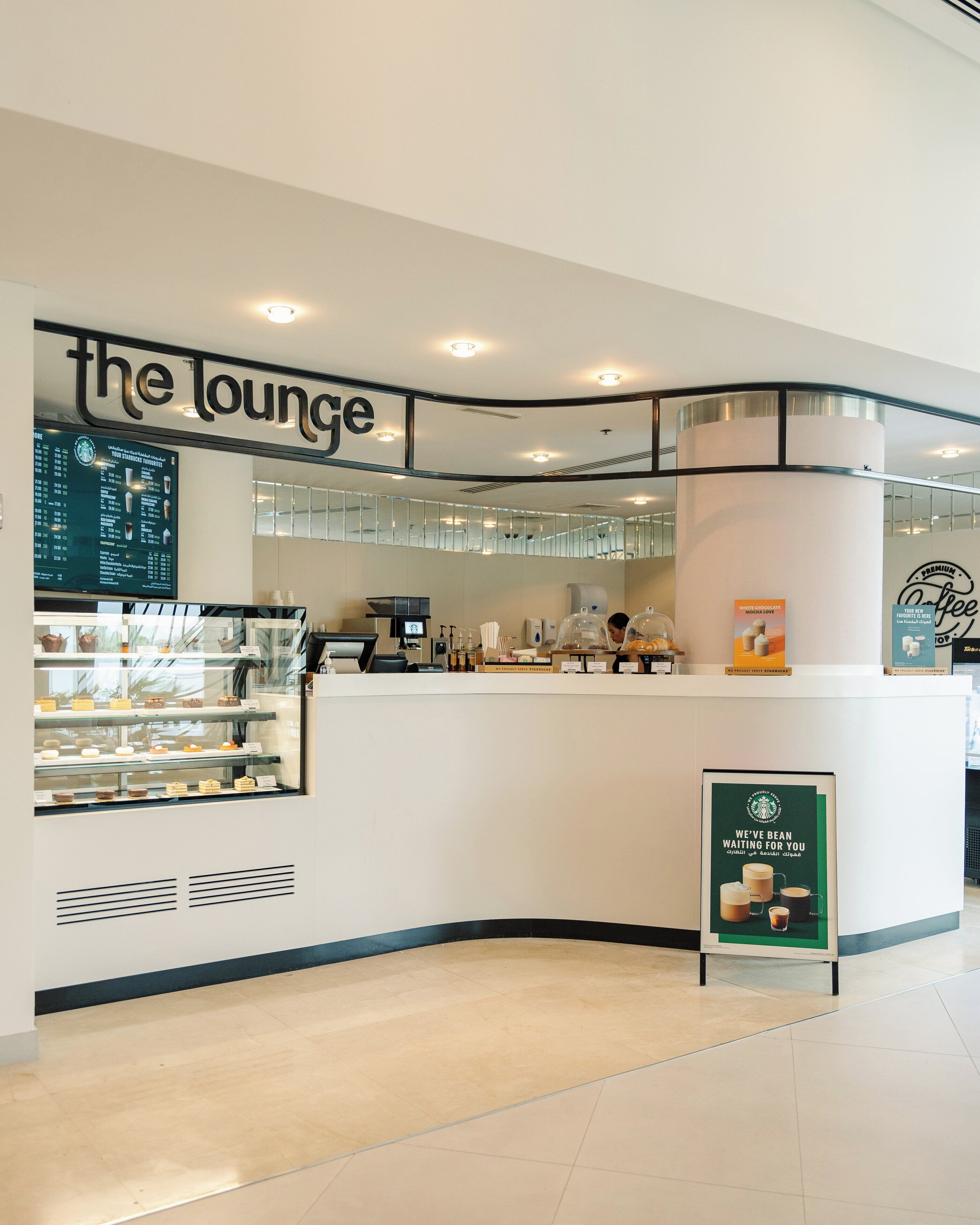Una tienda Starbucks con un mostrador curvo, tablero de menú y vitrinas con pasteles.