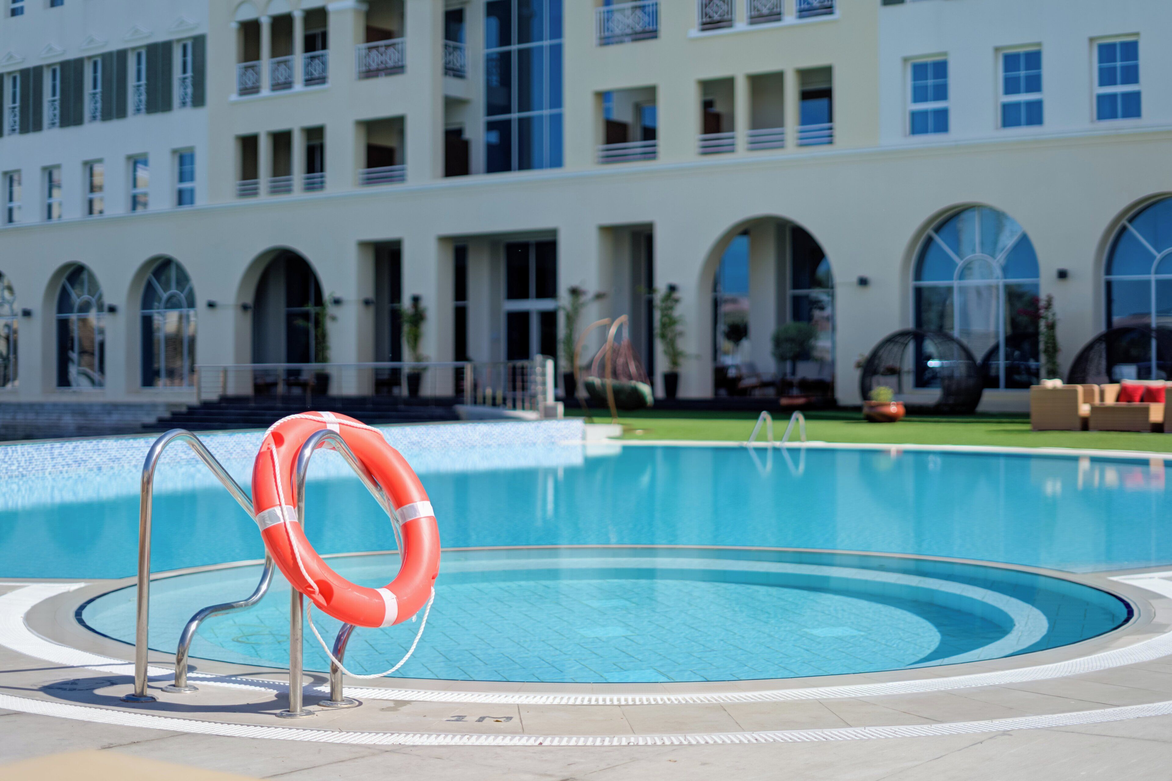 A swimming pool with a lifebuoy, surrounded by a building with arched windows and balconies.