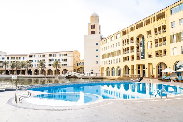 A swimming pool with a fountain, surrounded by buildings with balconies and arched windows. - Millennium Lakeview Hotel (Dubai)
