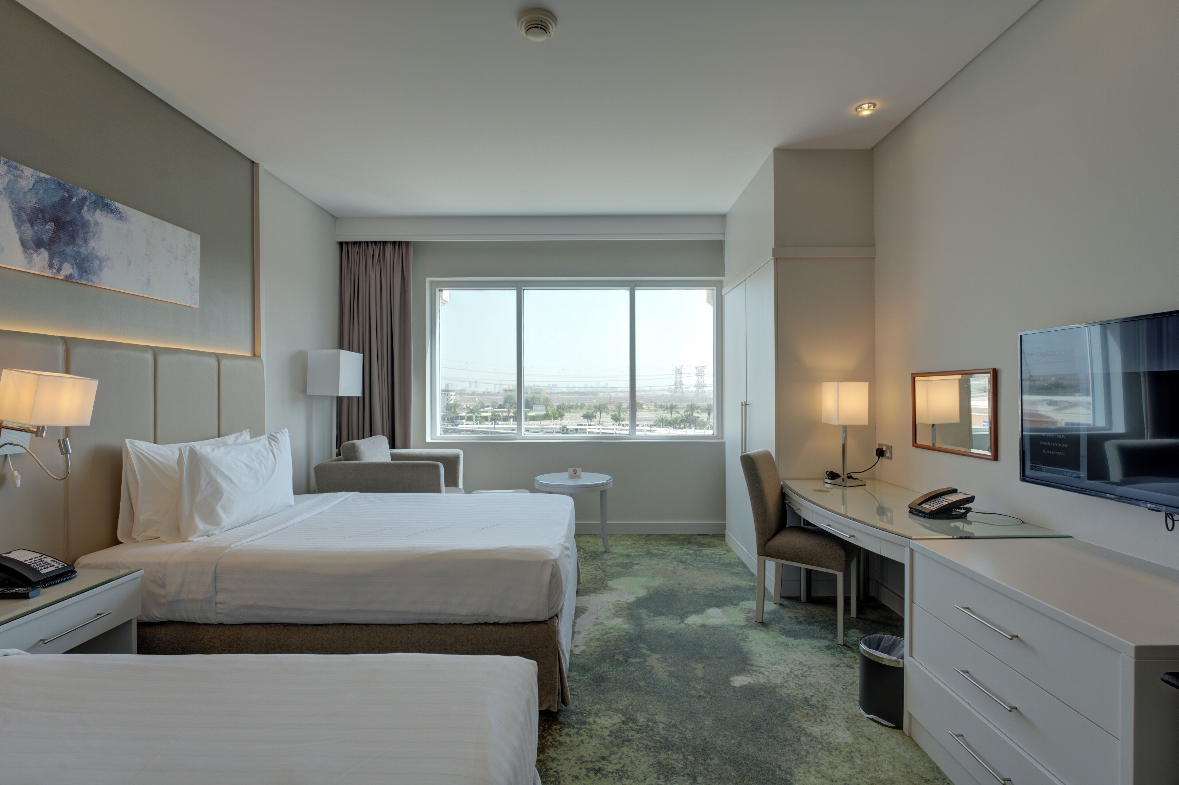 A hotel room with two beds, a desk, a chair, a TV, and a window with a city view.