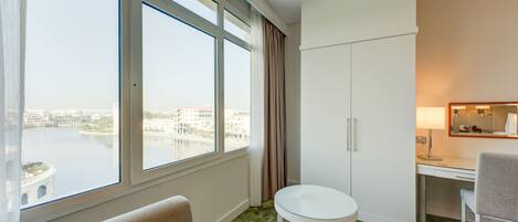 A hotel room with a large window, a desk, a chair, and a small round table.