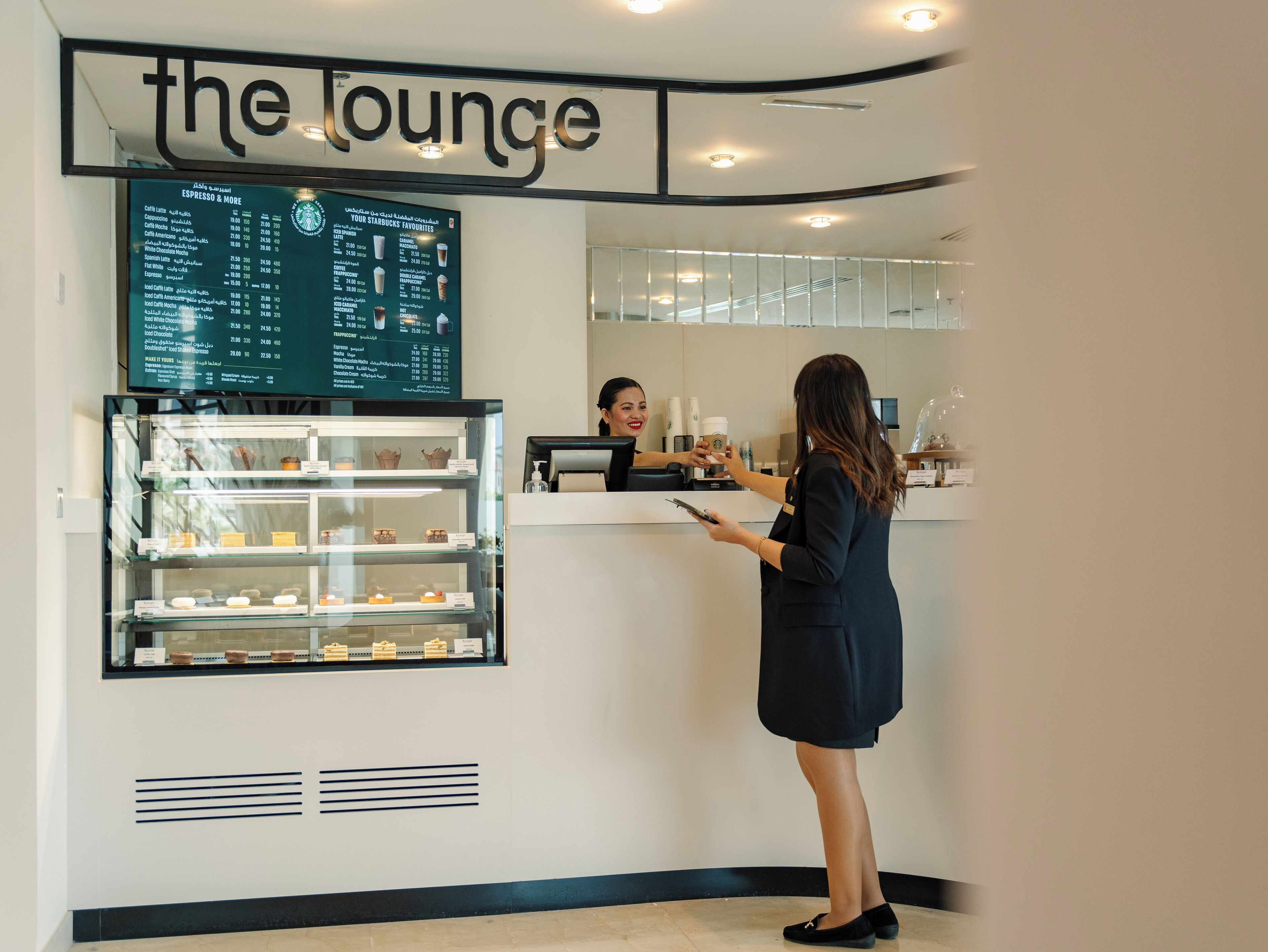 A Starbucks lounge with a menu board, a display case with pastries, and a counter where a customer is interacting with a barista.