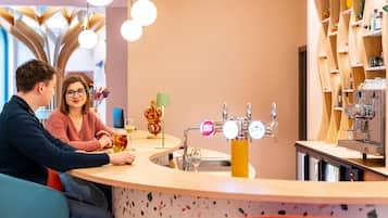 Een bar met een toonbank, een koffieapparaat en een plank met flessen.