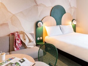 A hotel room with a bed, a sofa, a chair, and a table with a magazine. - ibis Styles Strasbourg Centre République (Strasbourg)