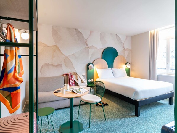A hotel room with a bed, a small table with a chair, a coat rack, and a window with curtains. - ibis Styles Strasbourg Centre République (Strasbourg)