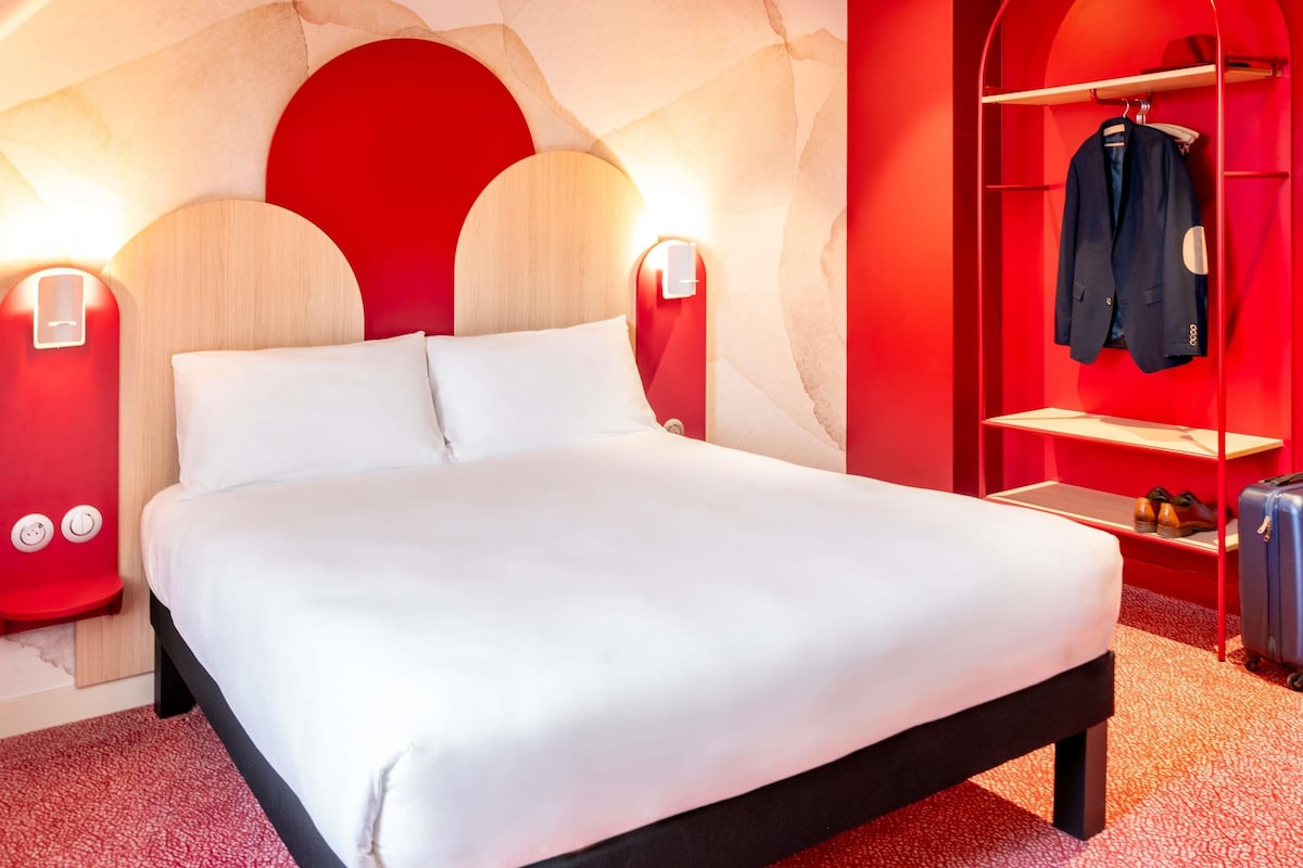 Una habitación de hotel moderna con una cama grande, un armario rojo y un zapatero.