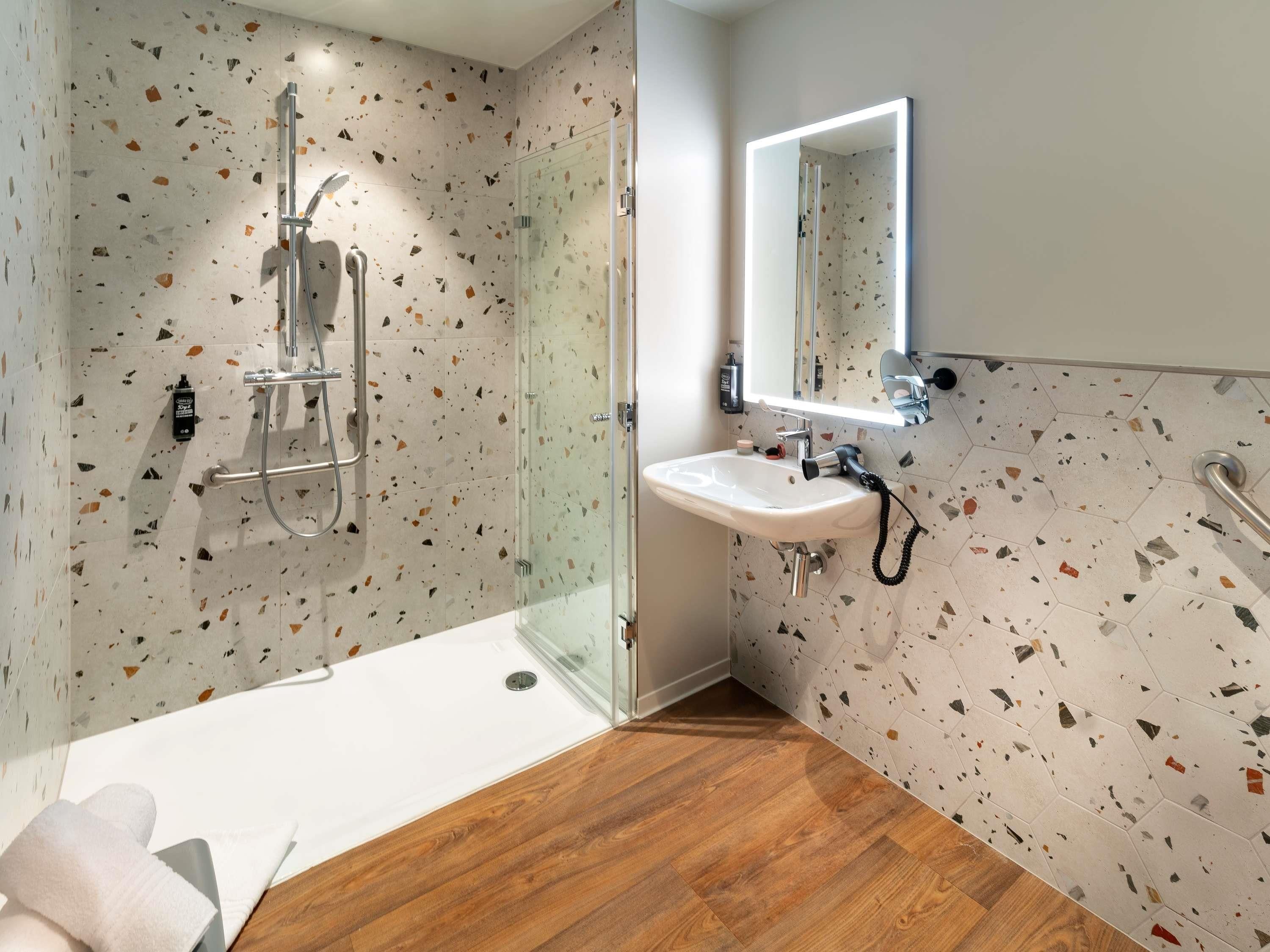 Ein modernes Badezimmer mit Duschkabine aus Glas, einem weißen Waschbecken und einem Spiegel mit integrierter Beleuchtung.