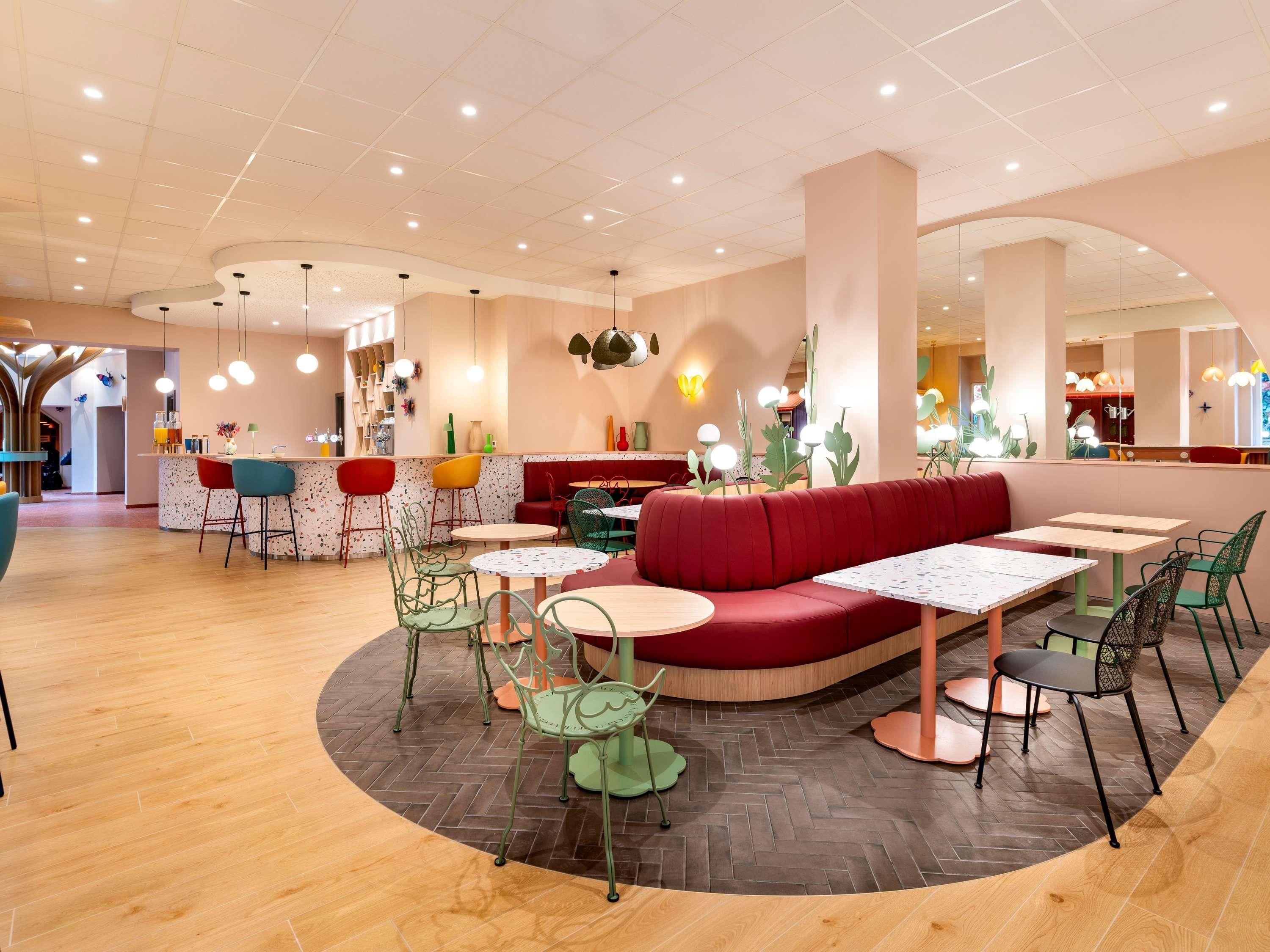 Um interior de restaurante moderno, com uma área de estar central vermelha, várias mesas e um balcão de bar.