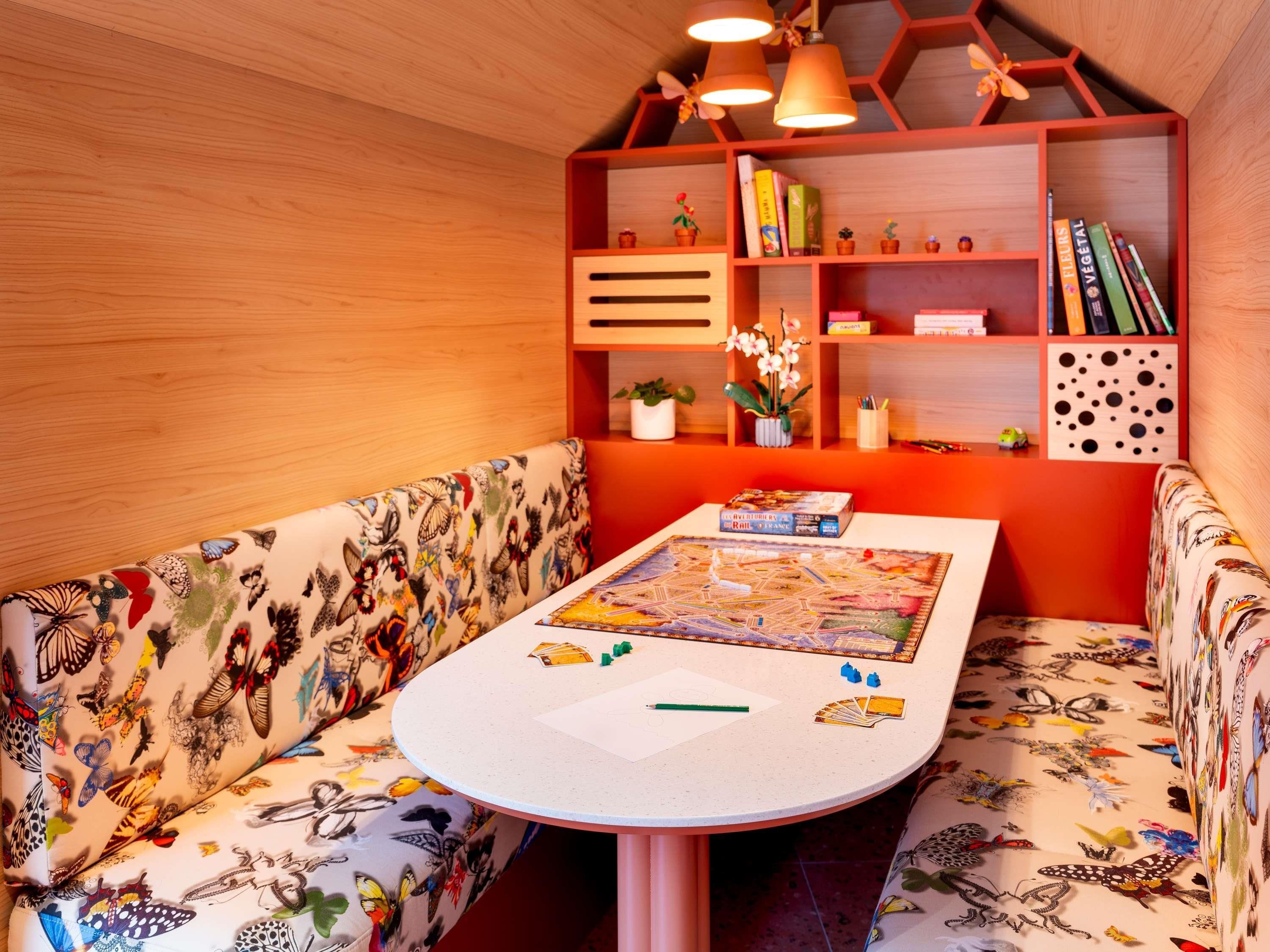 Um espaço de estar acolhedor com uma mesa redonda, rodeado por uma parede de madeira com padrão hexagonal e uma estante com diversos objetos.