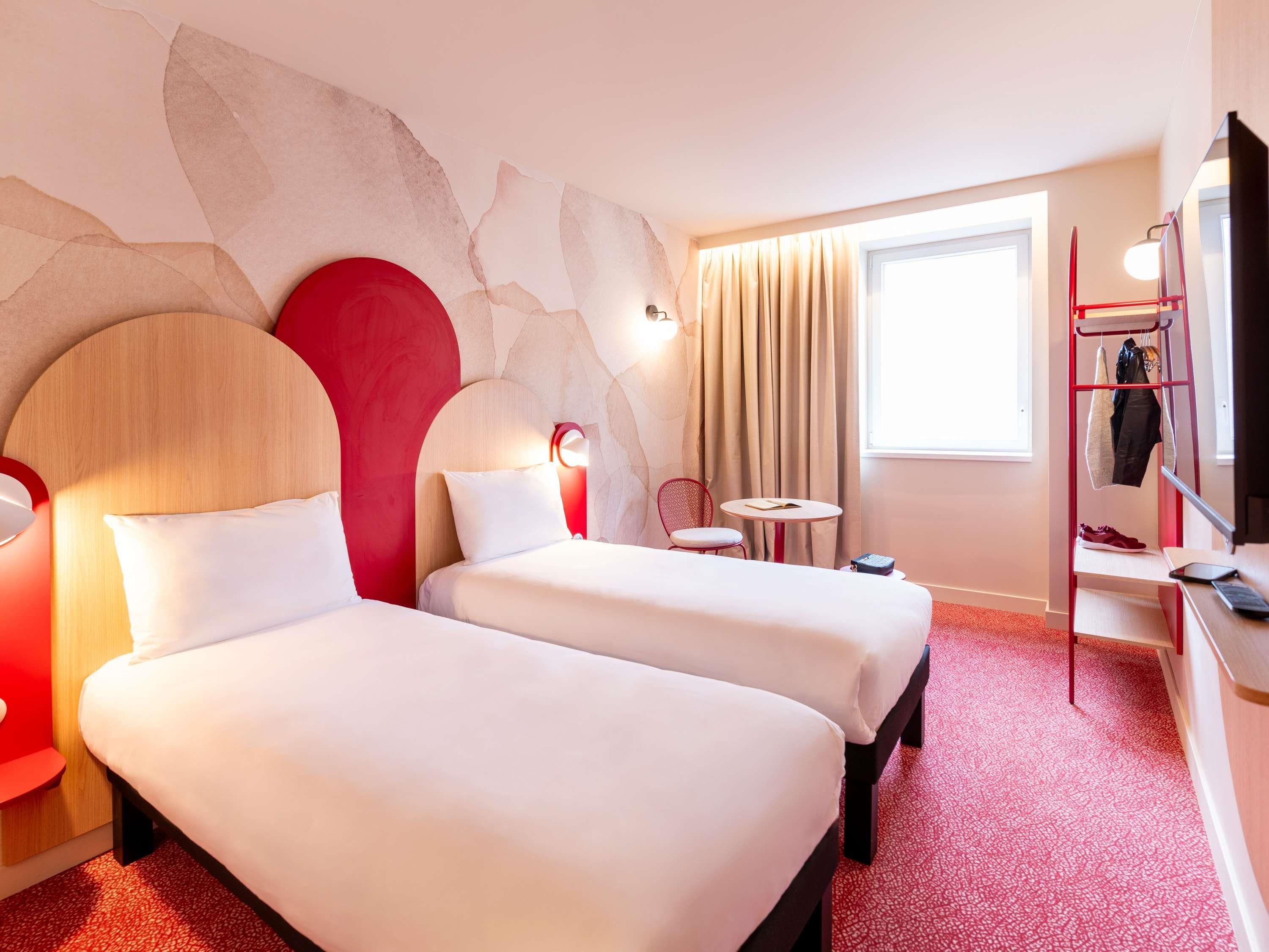 Habitación de hotel con dos camas, una mesita, una silla, televisión y ventana con cortinas.