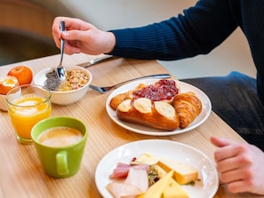 A breakfast setting with a plate of croissants, a bowl of cereal, a glass of orange juice, and a cup of coffee.