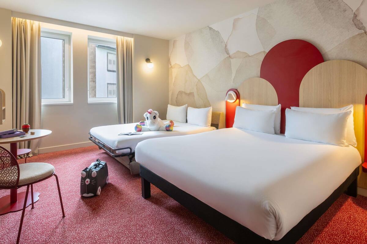 A hotel room with two beds, a small table, a chair, and a decorative wall.