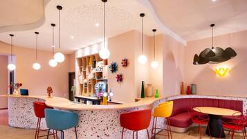 Een moderne bar met een gebogen toonbank, kleurrijke barkrukken en een zithoek met een ronde tafel en rode stoelen.