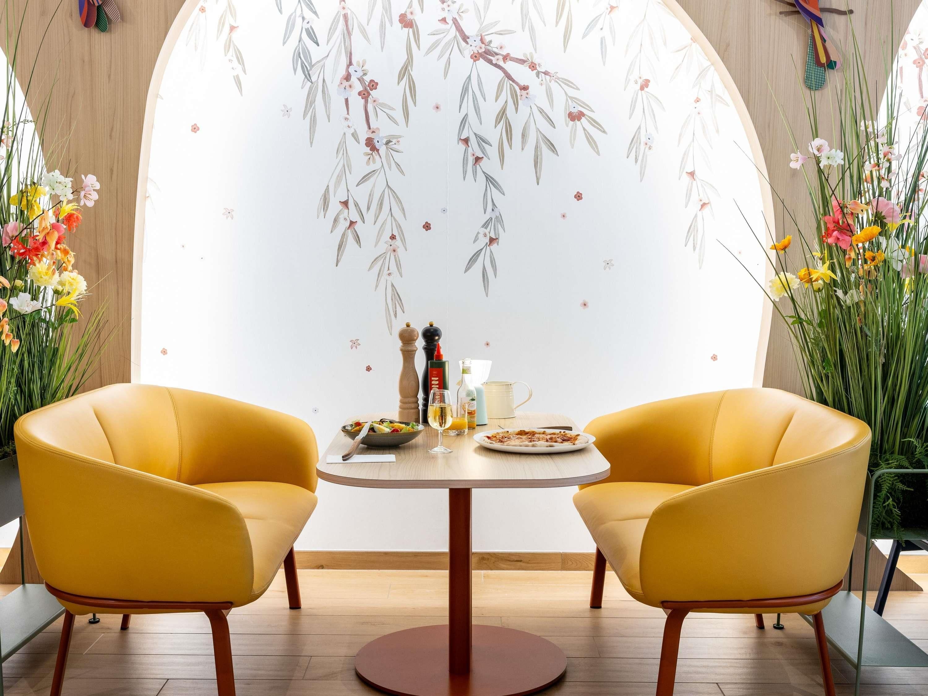 A dining area with two yellow chairs, a round table, and a floral wall mural.
