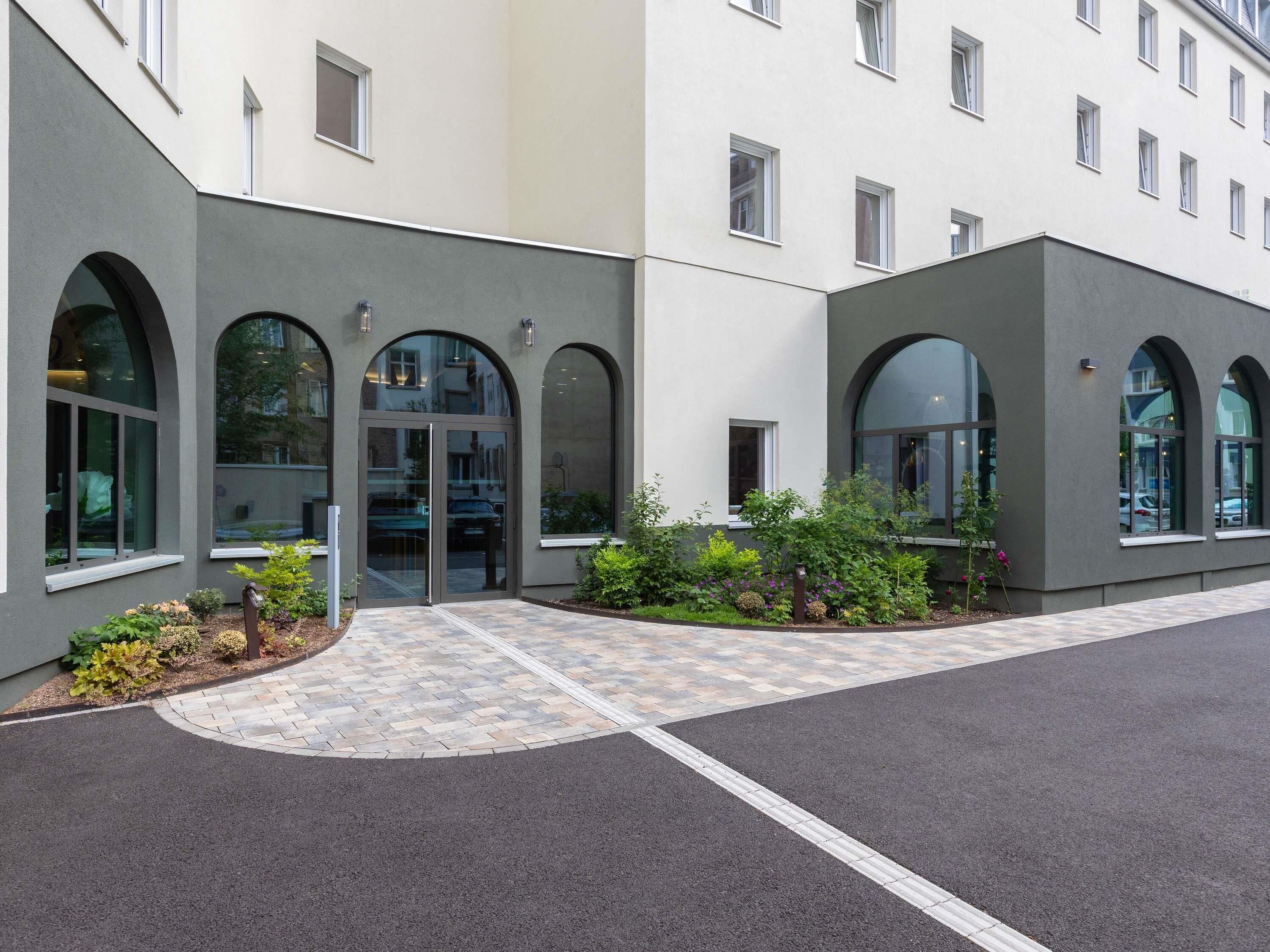 Un edificio moderno con ventanales arqueados y un área de acceso empavedada.