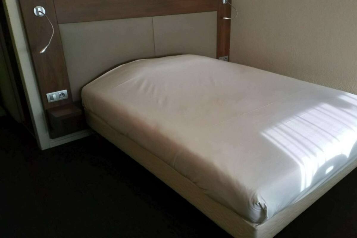 A single bed with a headboard, a bedside table, and a wall-mounted light fixture.