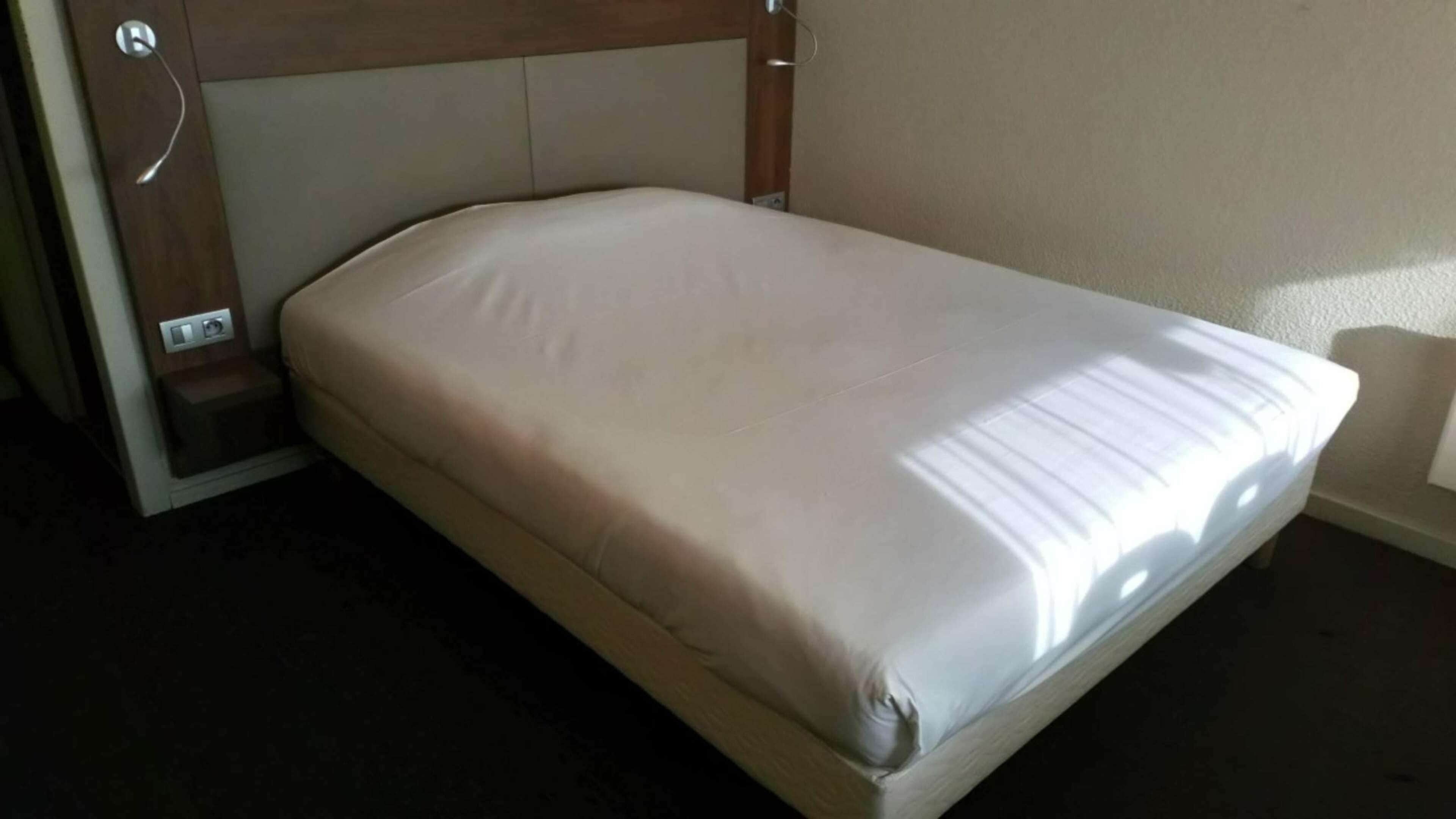 Una cama individual con cabecera, una mesita de noche y una lámpara de pared.