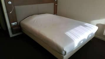 Una cama individual con cabecera, una mesita de noche y una lámpara de pared.