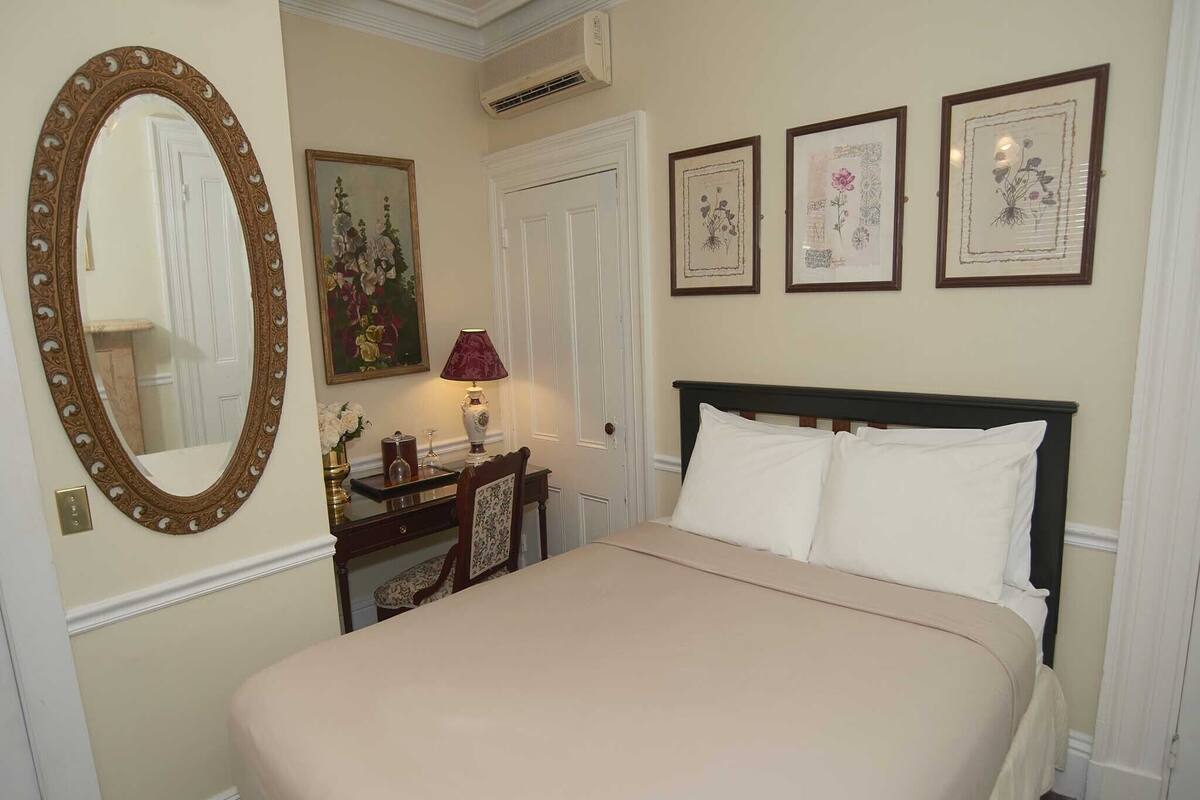 A neatly arranged bedroom with a large bed, a dresser, a mirror, and three framed floral artworks on the wall.