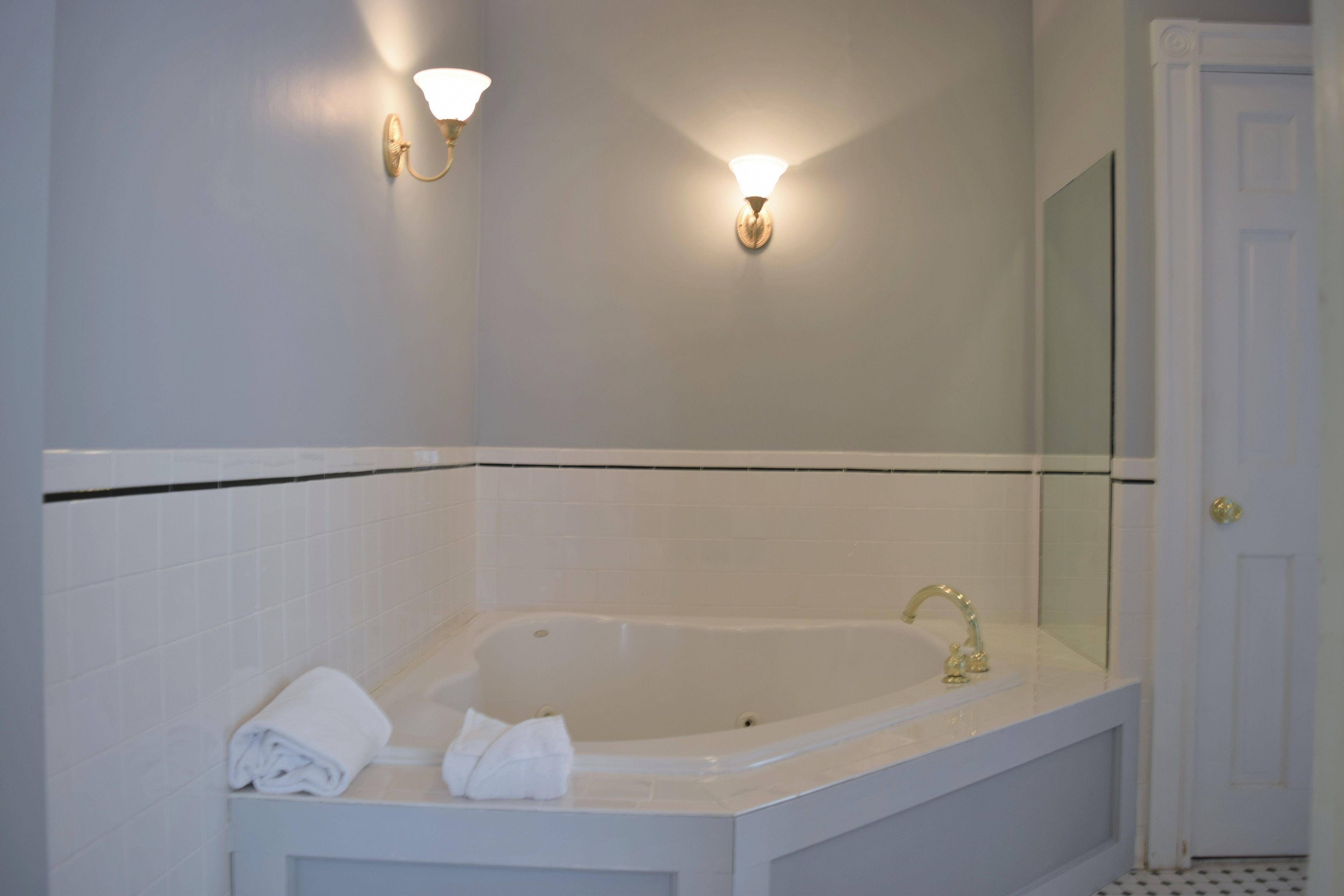 Un bagno con una vasca da bagno bianca, due luci a parete e una porta bianca.