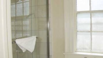A bathroom with a glass shower enclosure, a toilet, and a window with a floral curtain.