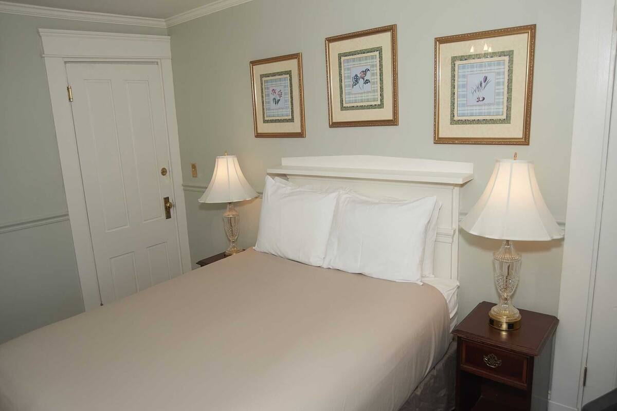 A neatly made bed with white linens, two bedside tables with lamps, and three framed pictures on the wall.