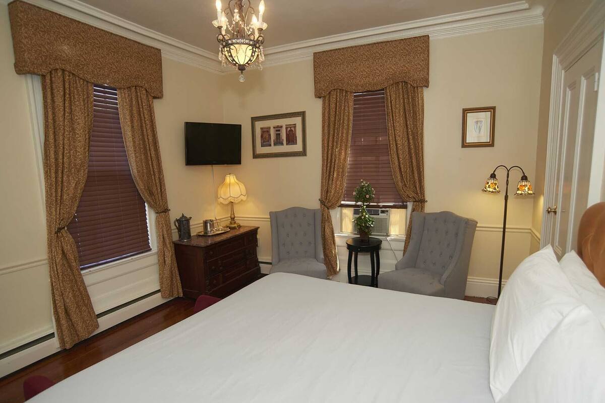 A hotel room with a large bed, two armchairs, a small table with a lamp, a television, and a floor lamp.