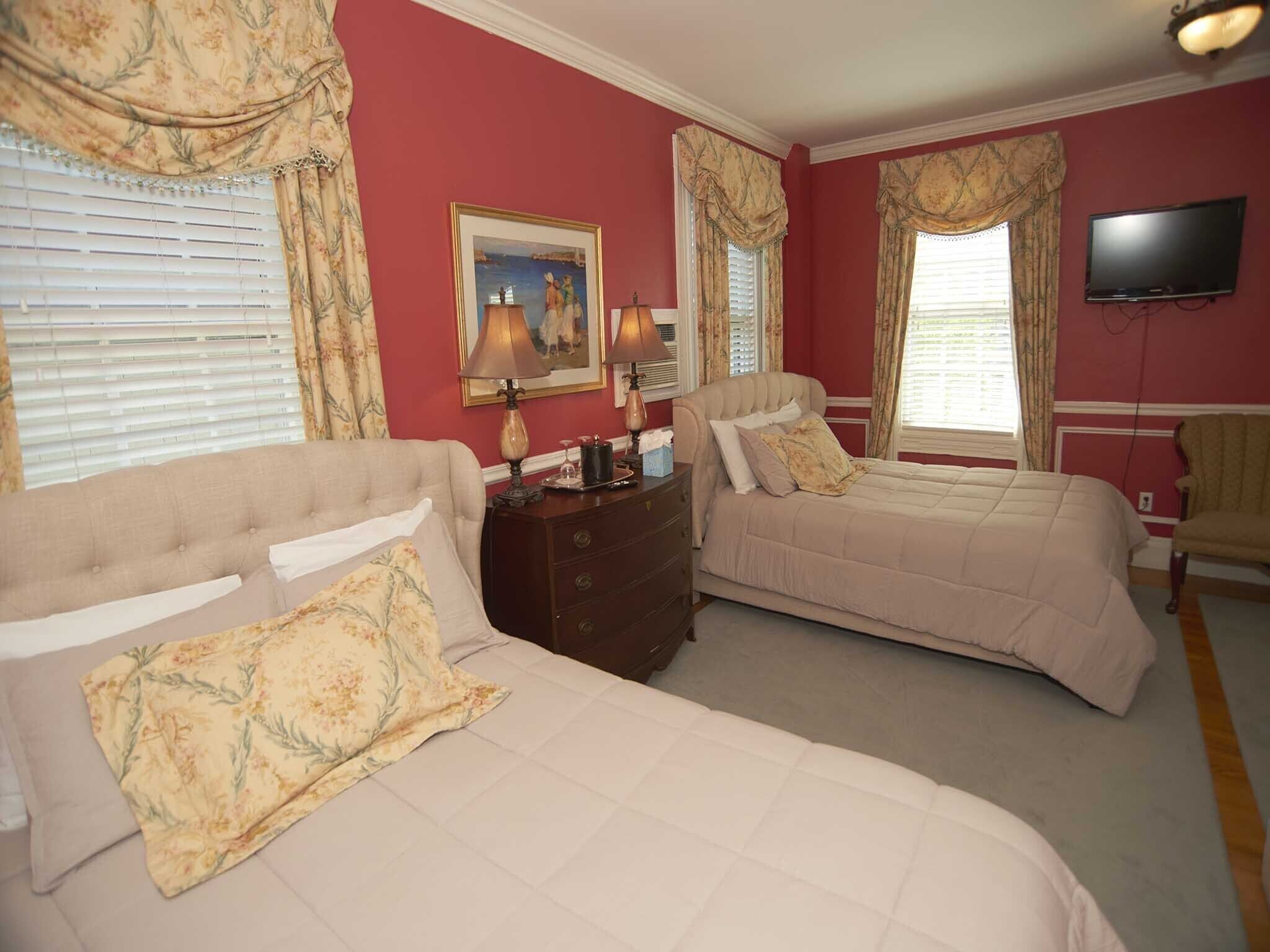 A hotel room with two beds, a dresser, a television, and a painting on the wall.