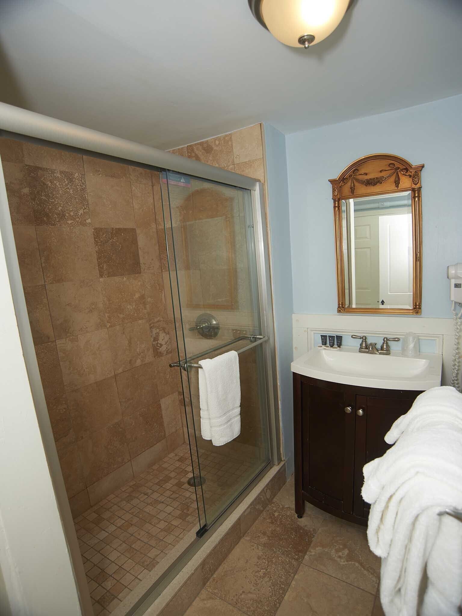 A bathroom with a glass shower enclosure, a sink with a mirror above it, and a towel rack with a white towel.