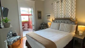 A bedroom with a large bed, bedside lamps, a chair, a small table, and a potted plant.