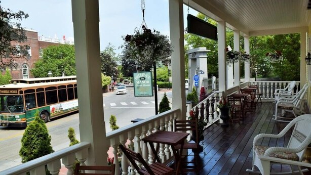 Eine überdachte Veranda mit Holzmöbeln und Blick auf eine Straße mit einem Bus.