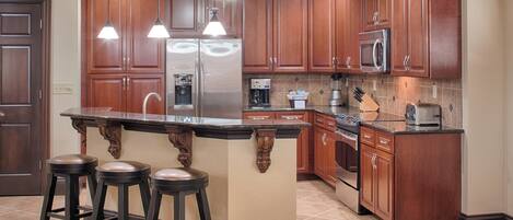 A kitchen with wooden cabinets, a stainless steel refrigerator, a microwave, and a central island with stools.