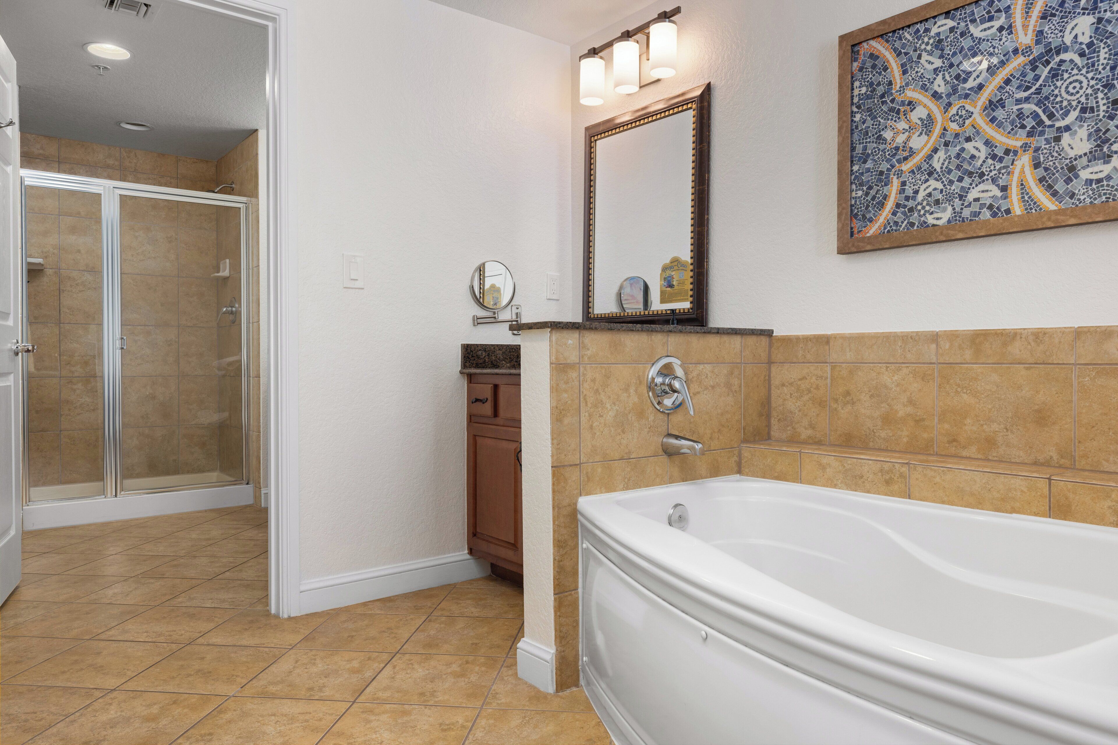 Une salle de bain équipée d’une baignoire, d’une douche, d’un meuble-lavabo avec un miroir et d’une œuvre d’art en mosaïque sur le mur.