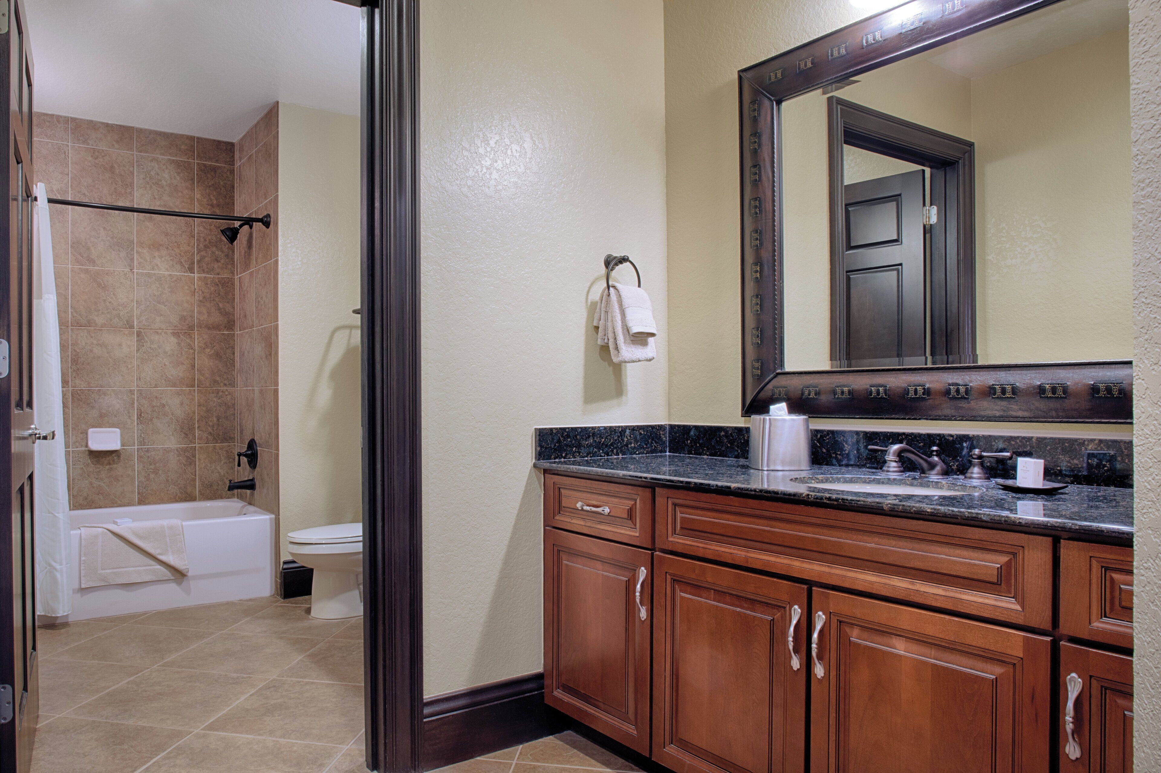 A bathroom with a bathtub, toilet, and sink, wooden cabinets, and a large mirror.