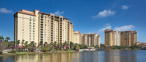 A high-rise hotel with multiple balconies, a waterfront view, and a reflection in the water.