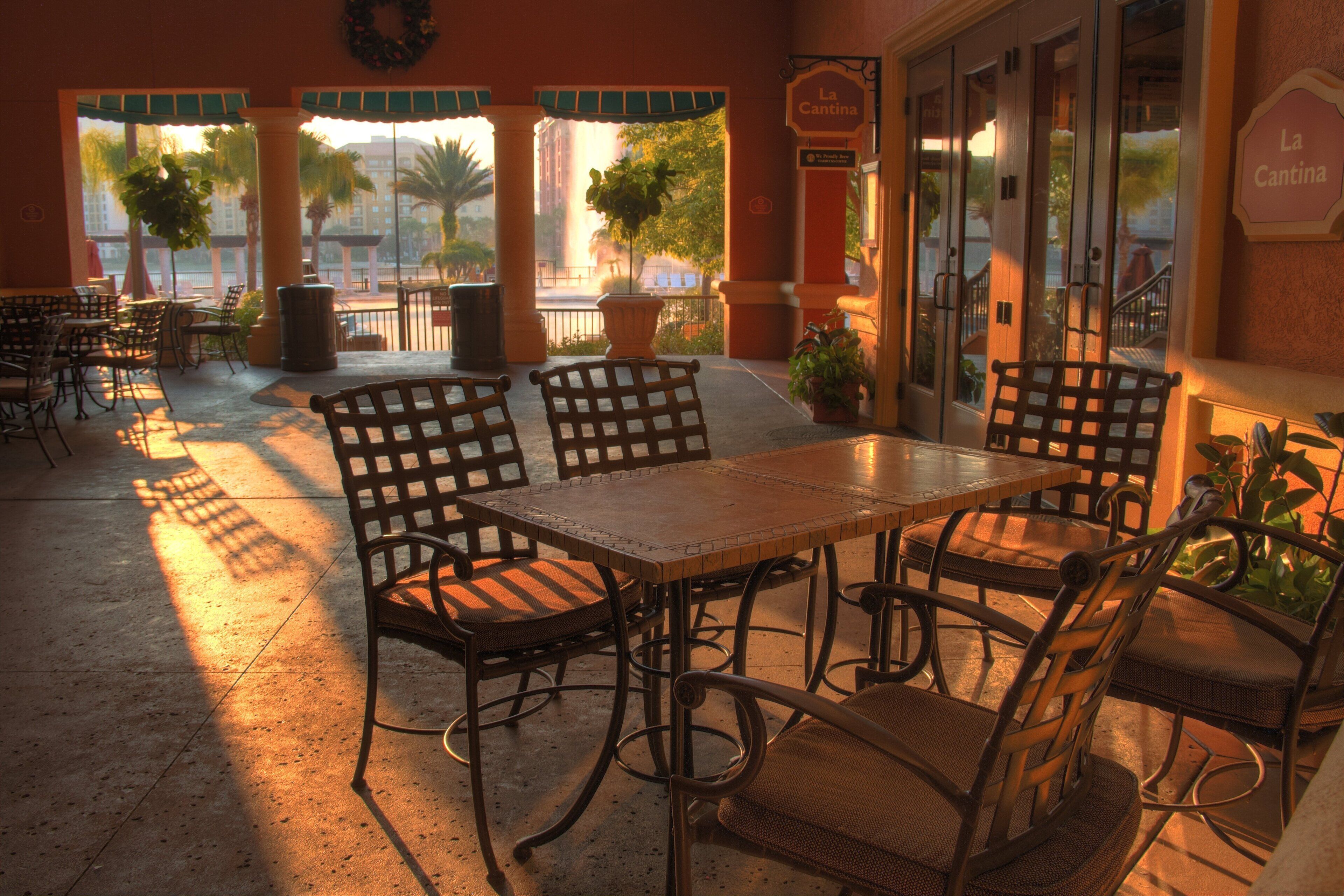 An outdoor patio with a table and chairs, potted plants, and a view of palm trees and buildings.