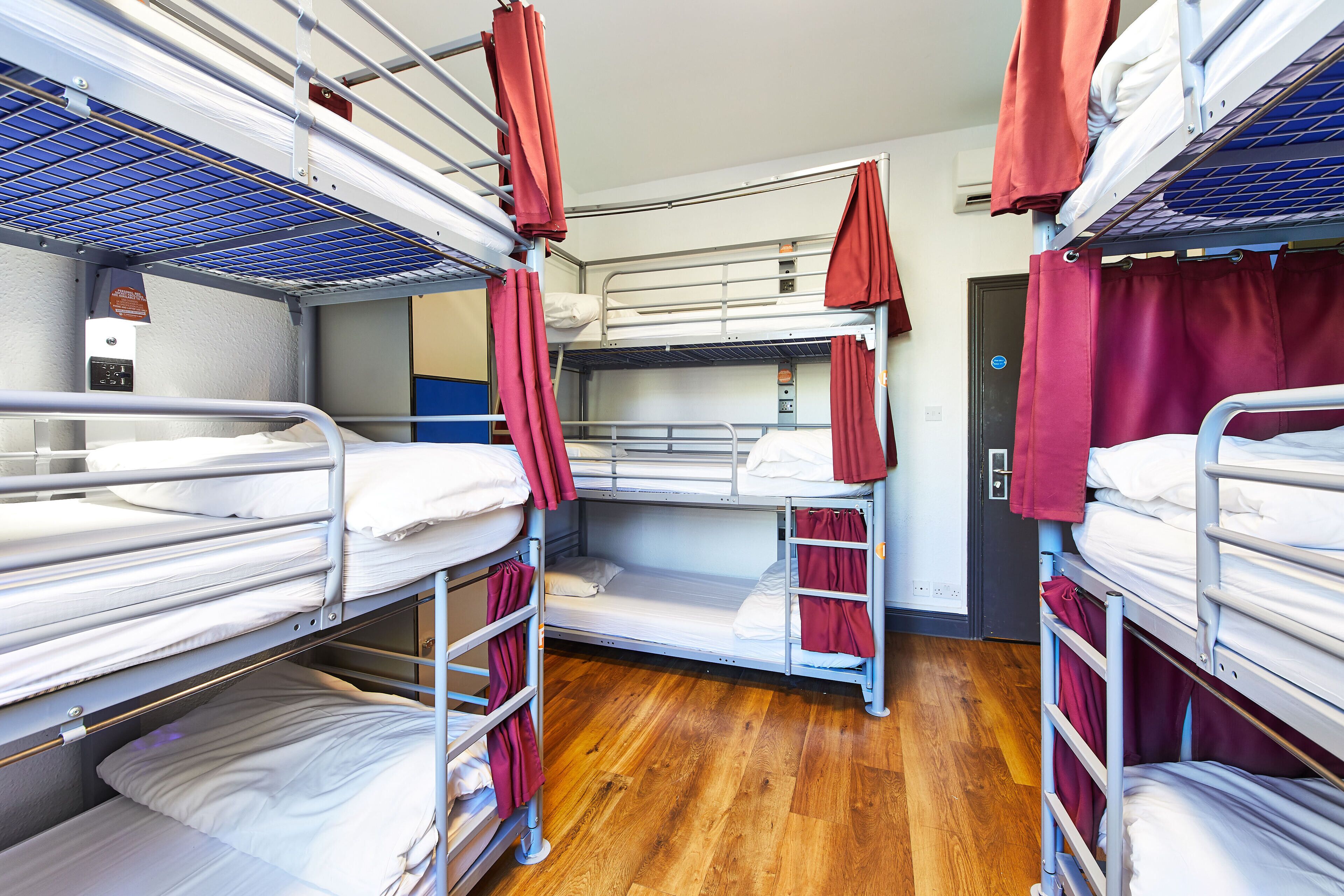 A bunk room with metal bunk beds, wooden flooring, and red curtains.