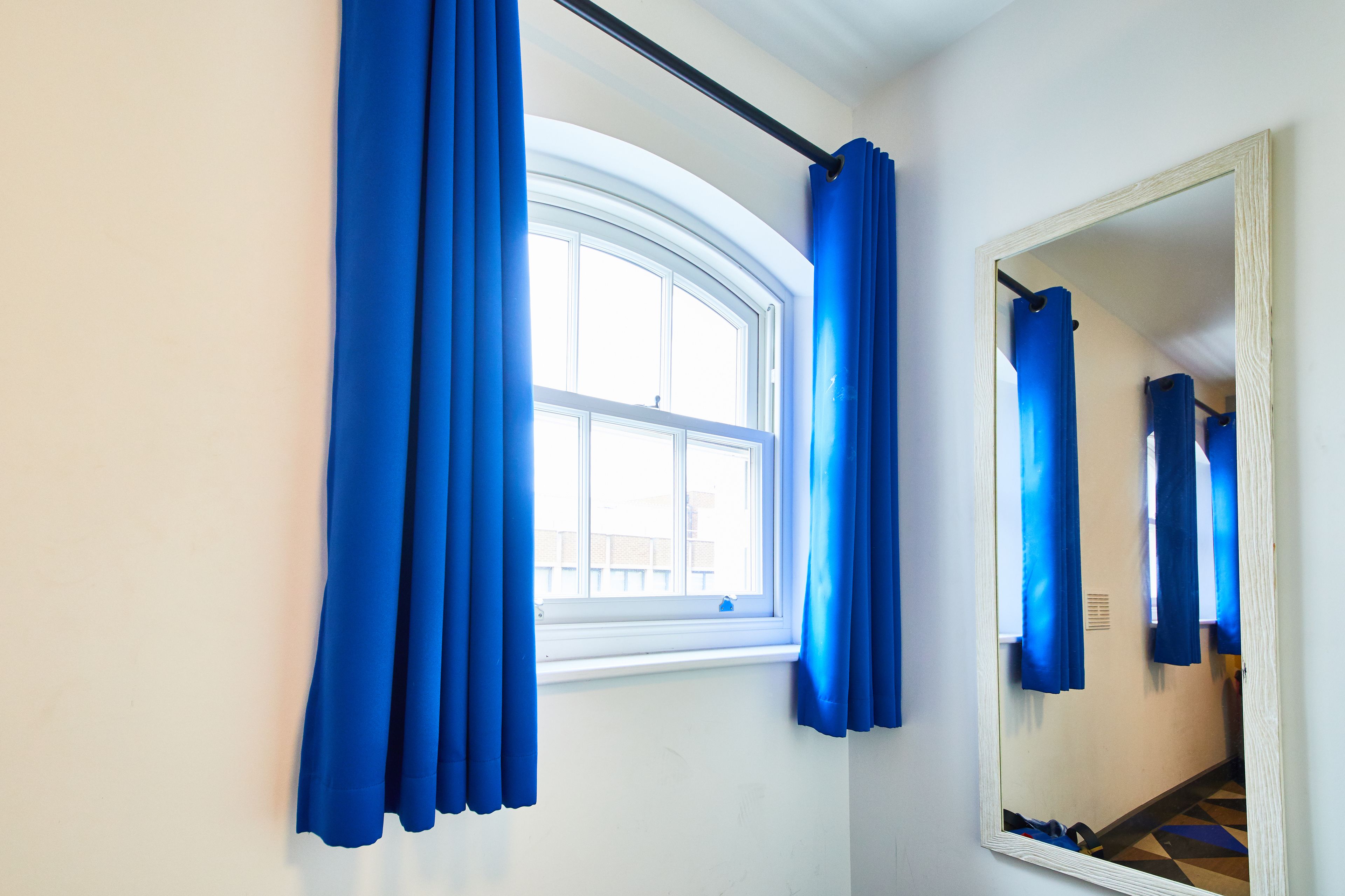 A room with a window, blue curtains, and a mirror.