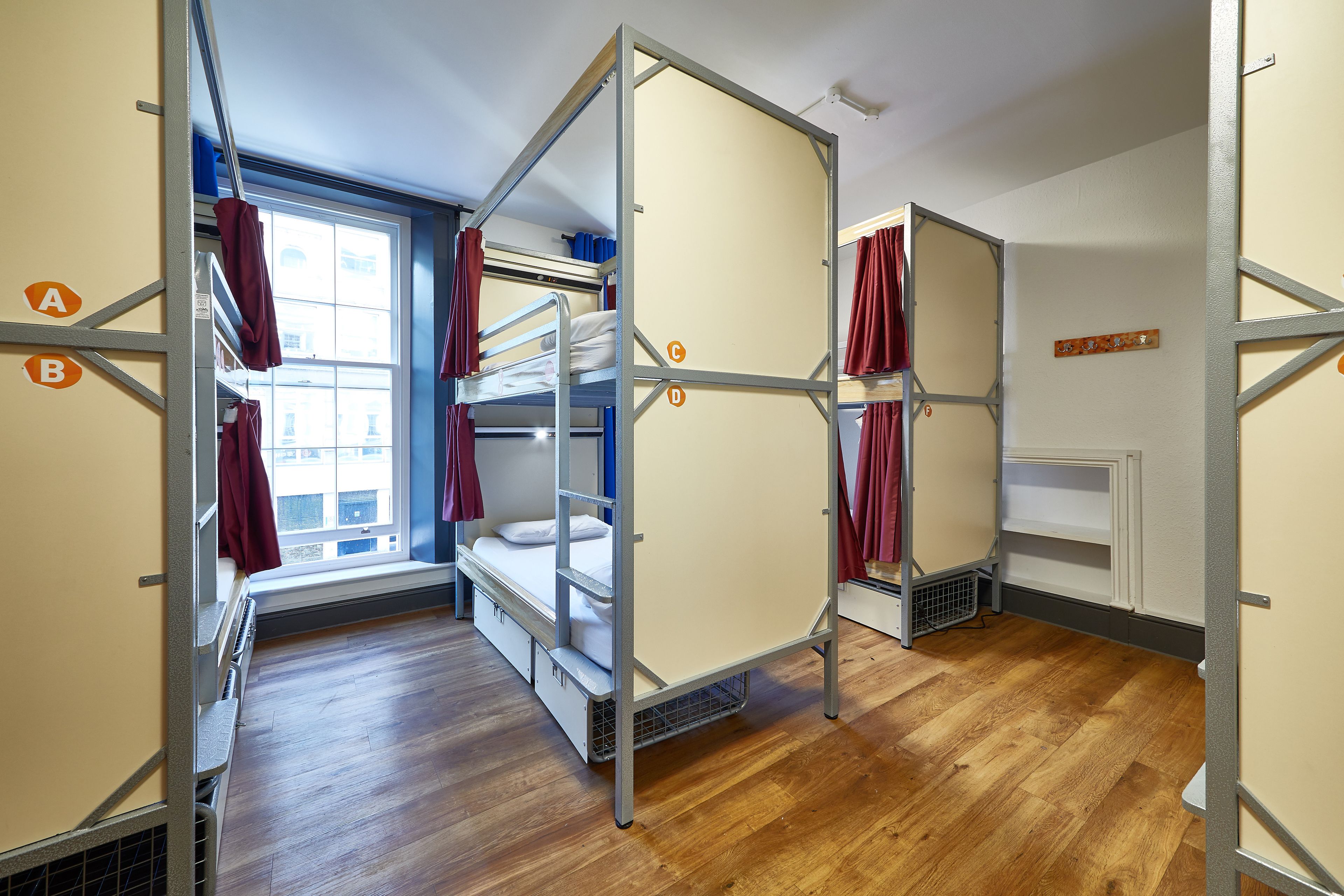A dormitory room with bunk beds, a window with curtains, and a radiator.