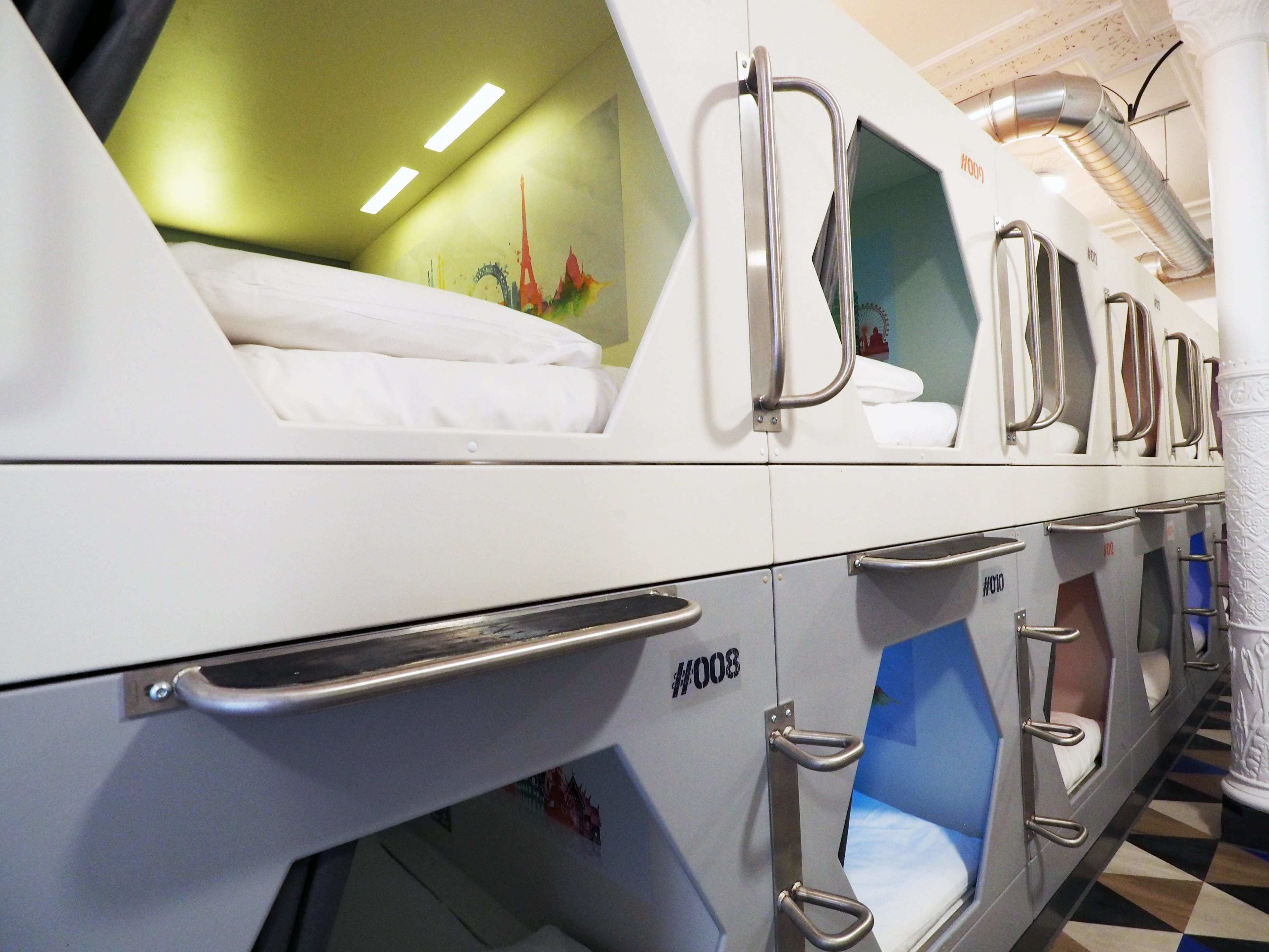 A row of bunk beds with metal handles, a green wall with a mural, and a patterned floor.