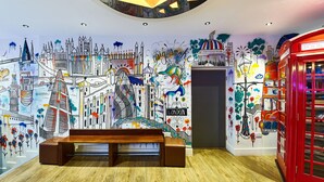 A room with a mural of London landmarks, a red telephone booth, and a bench. - St Christopher's Village, London Bridge - Hostel (London)