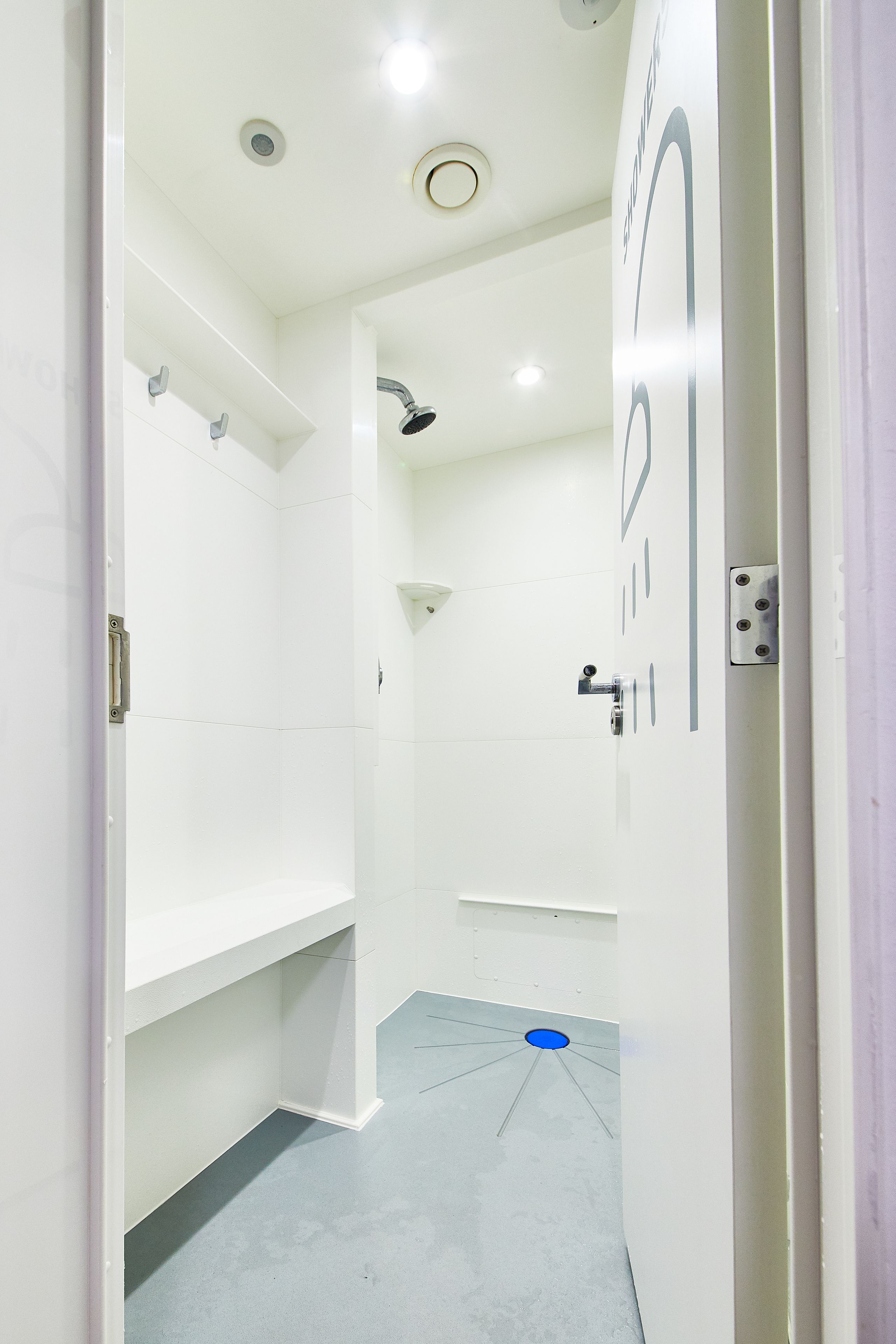 A modern bathroom with white walls, a shower, and a blue floor mat.