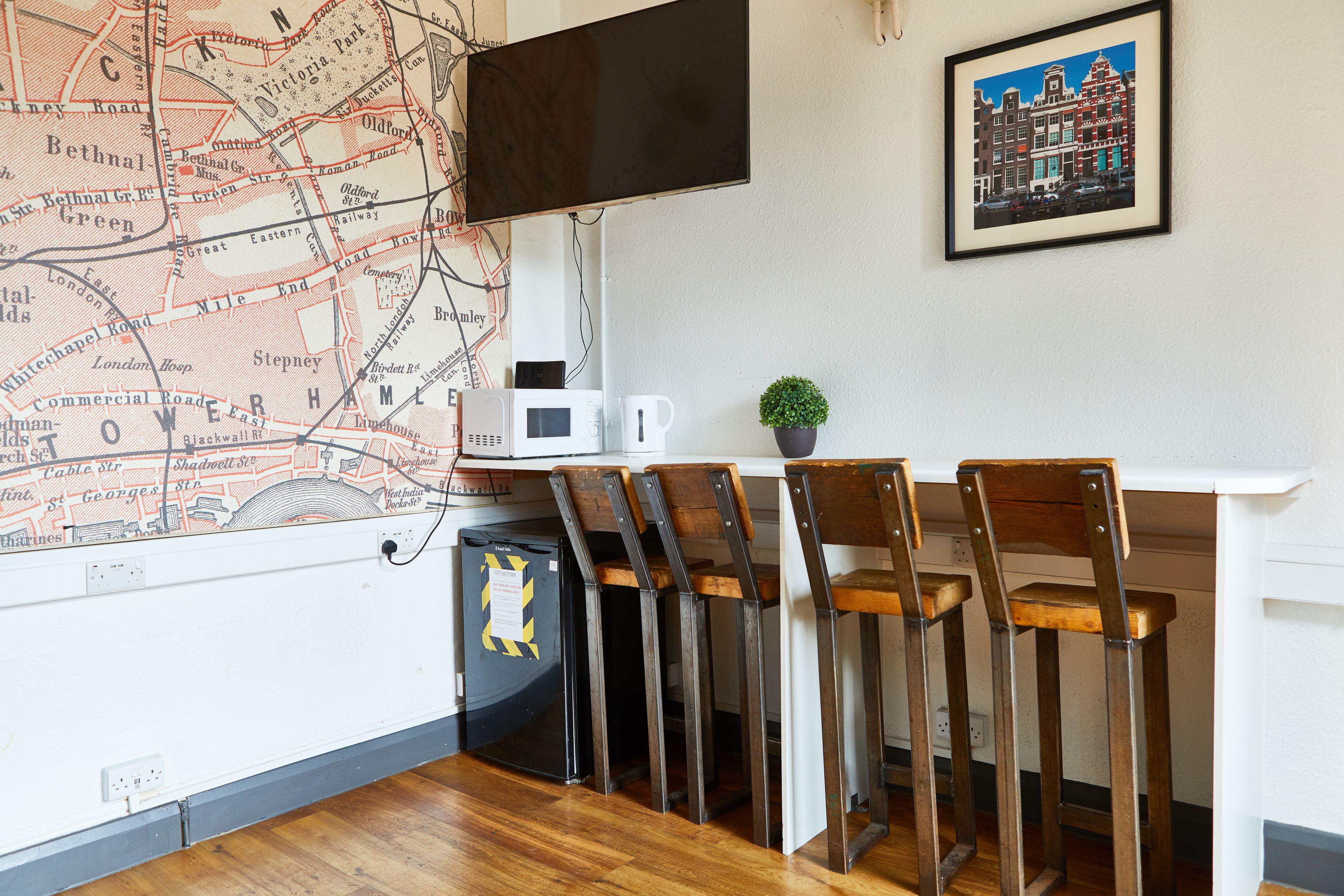 A room with a map on the wall, a television, a desk with chairs, and a small plant.