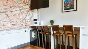 A room with a map on the wall, a television, a desk with chairs, and a small plant.
