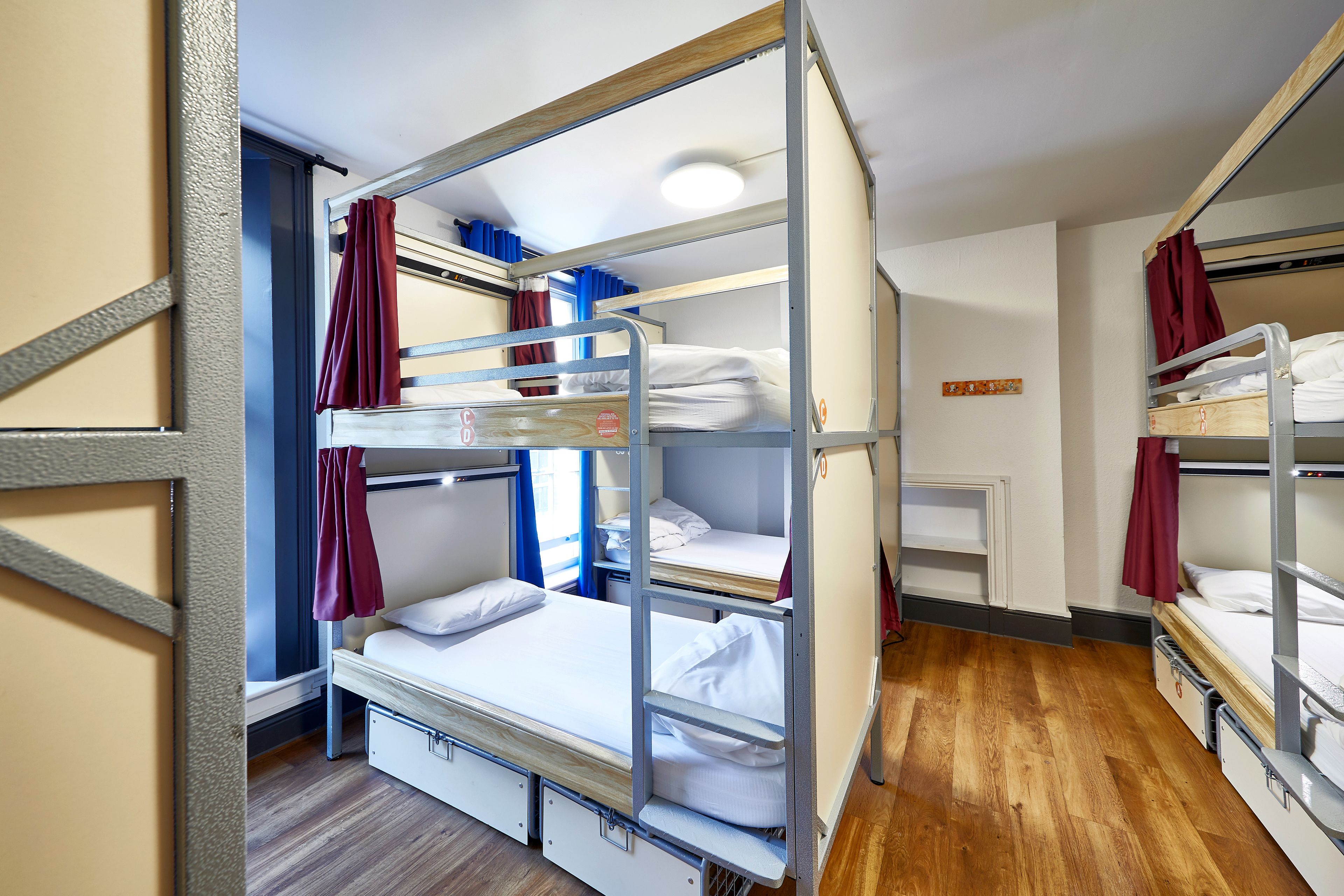 Une chambre avec un lit superposé, un plancher en bois, une porte blanche et un rideau rouge.