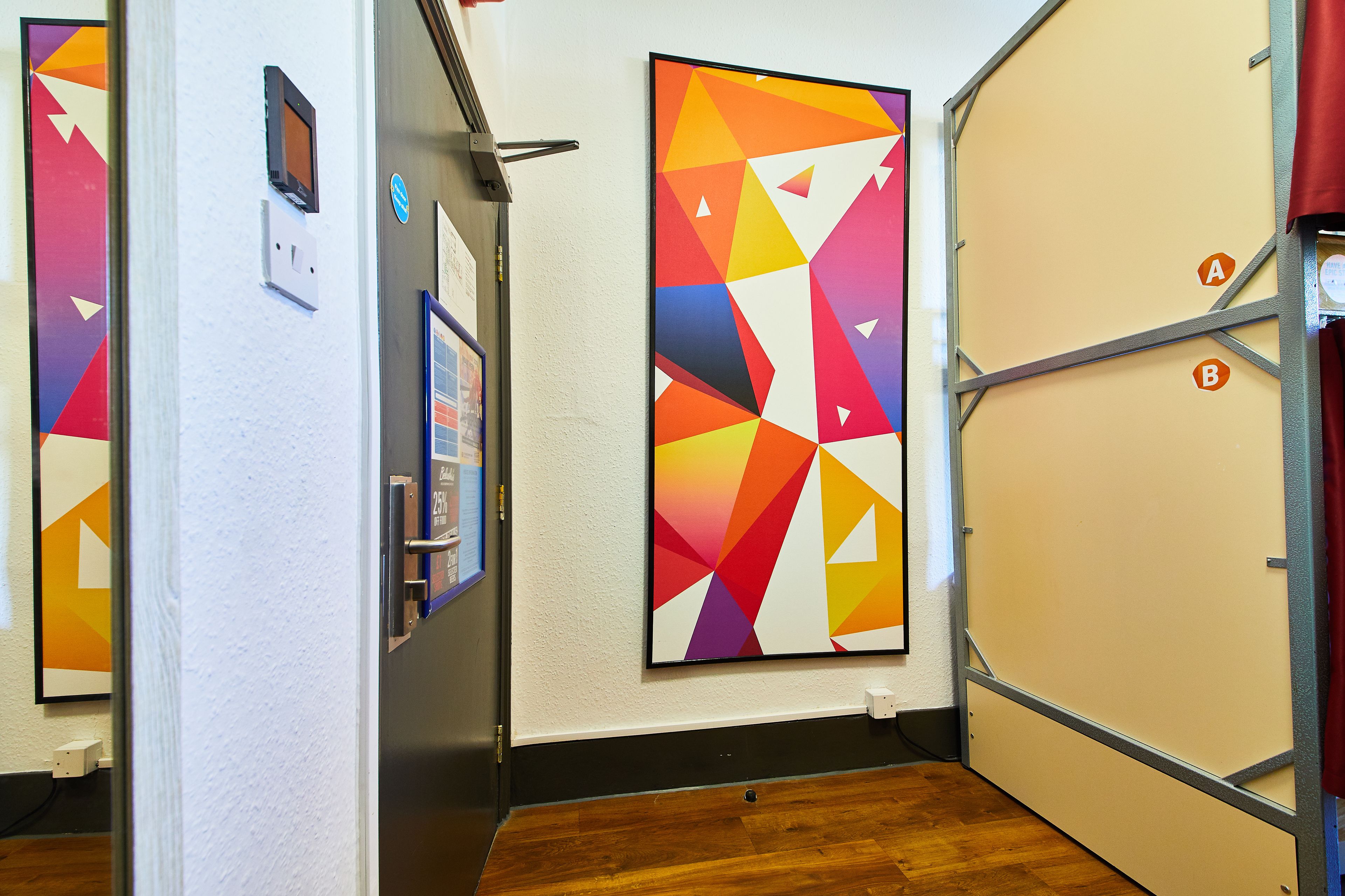 Een gang met een houten vloer, witte muren en kleurrijke geometrische kunstwerken.