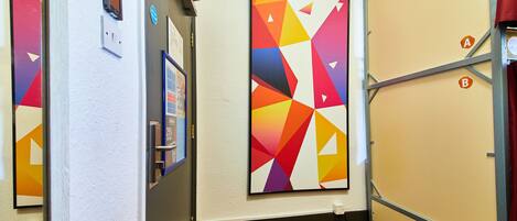 A hallway with a wooden floor, white walls, and colorful geometric artwork.
