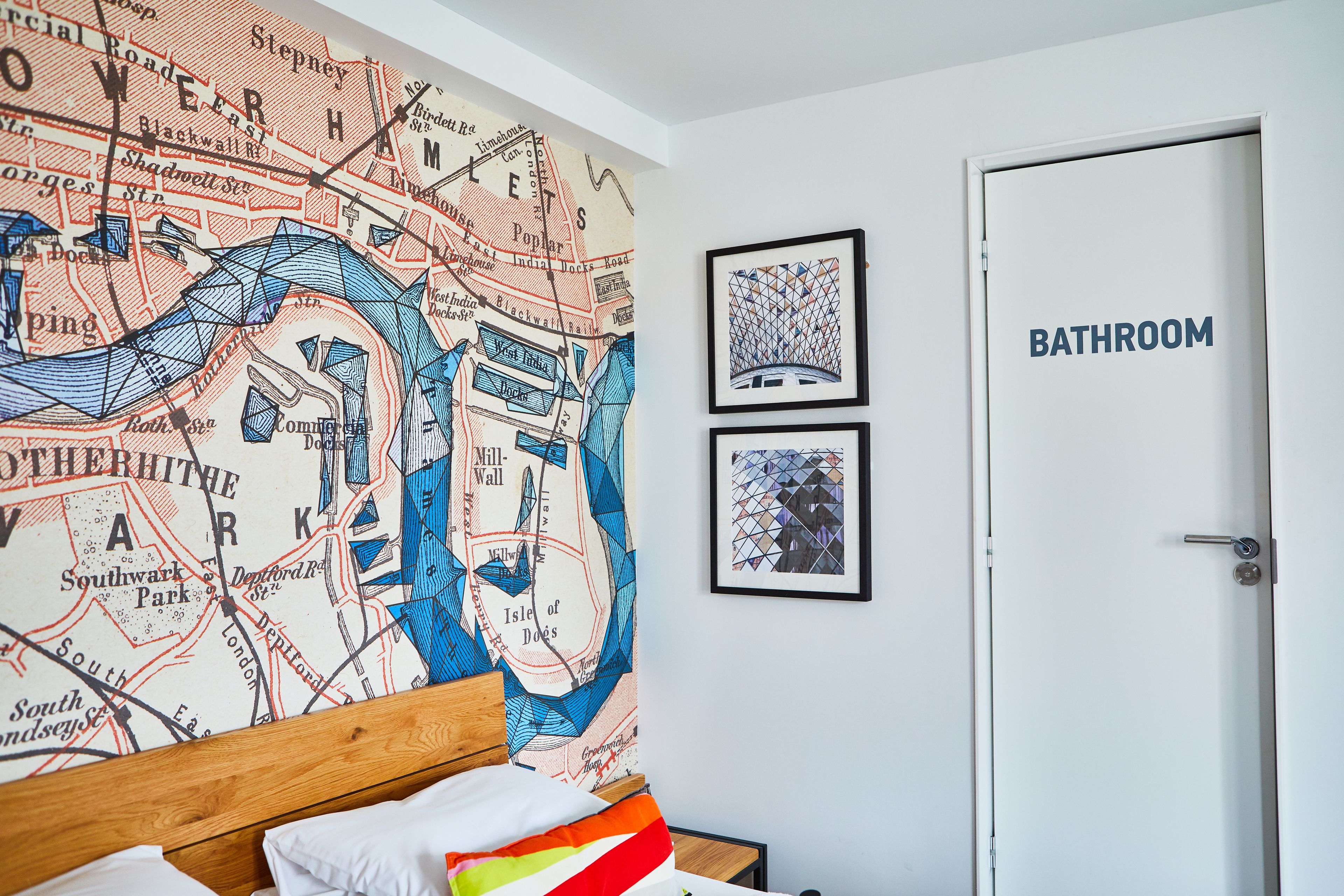 Una camera da letto con un murale raffigurante una mappa, un letto con cuscini e una porta con la scritta 'BATHROOM'.