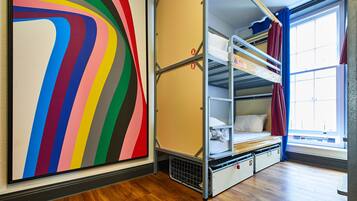 A room with bunk beds, a colorful abstract painting, and a window with curtains.
